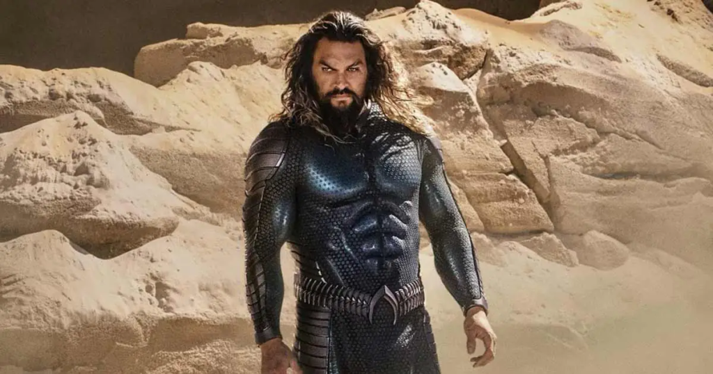 Aquaman, played by Jason Momoa, standing on a rock formation in front of a fiery underwater landscape, promoting the upcoming film 'Aquaman and the Lost Kingdom